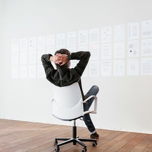 A man reclining in a white chair, facing a wall of ideas on notecards.