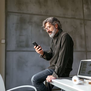 A man sitting at his desk, checking his phone with a smile.