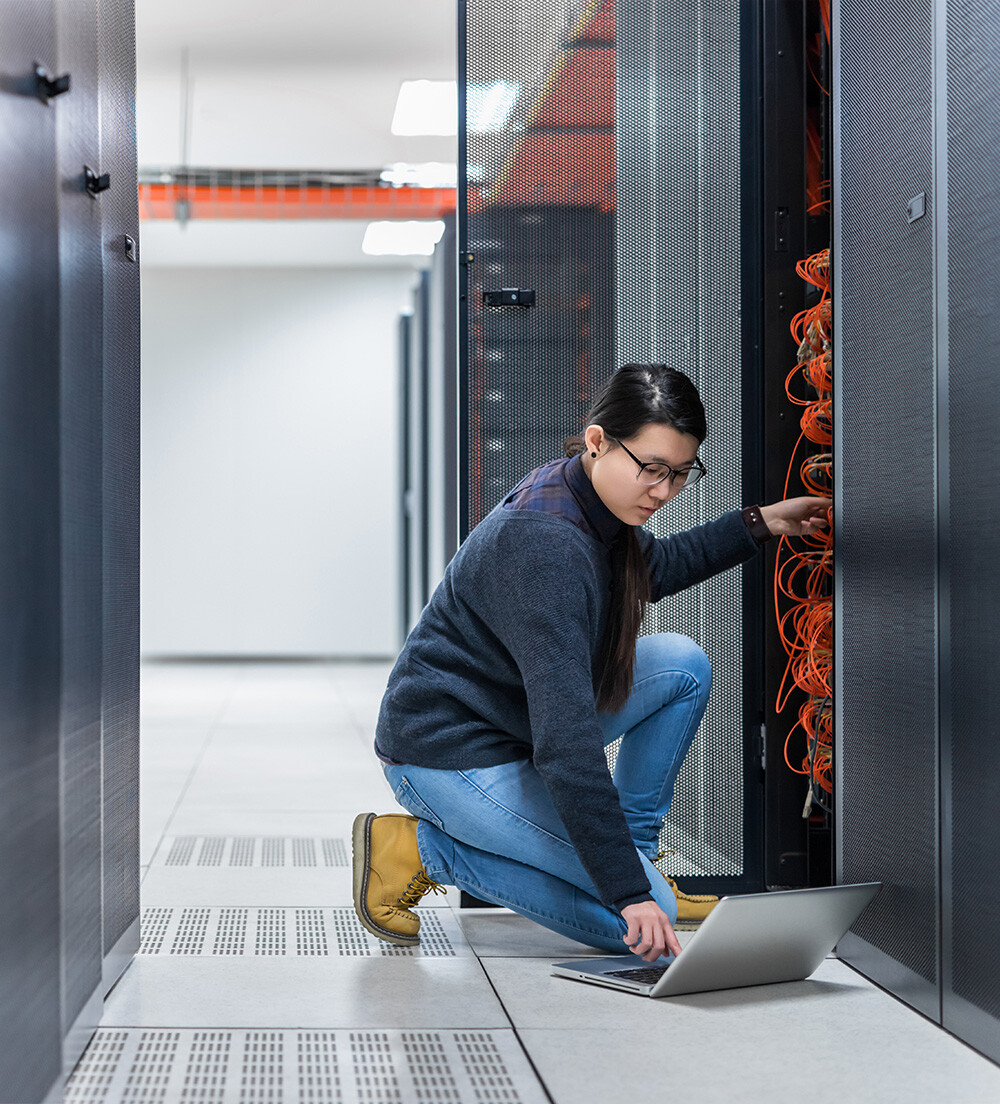 A woman inspecting IT datacenter hardware, scrolling her laptop for information.