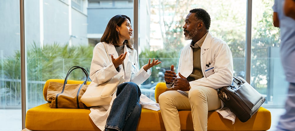 Two colleagues talking while sitting on a yellow ochre bench.