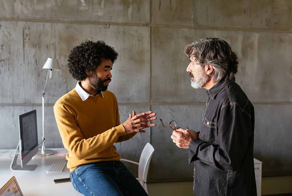 Two colleagues talk in the office, collaborating on a solution.