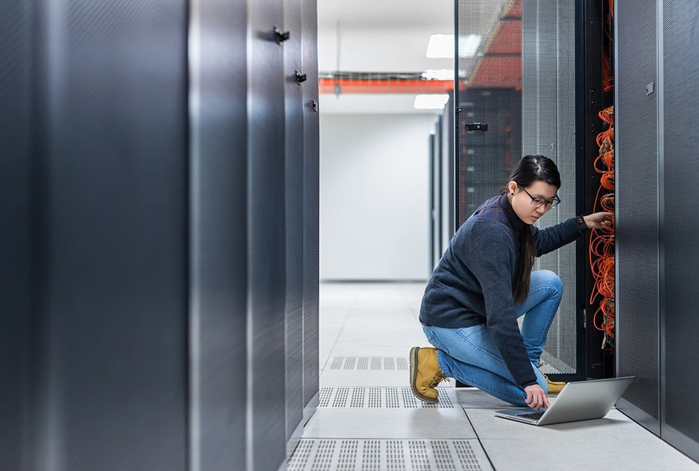 A woman inspecting IT datacenter hardware, scrolling her laptop for information.