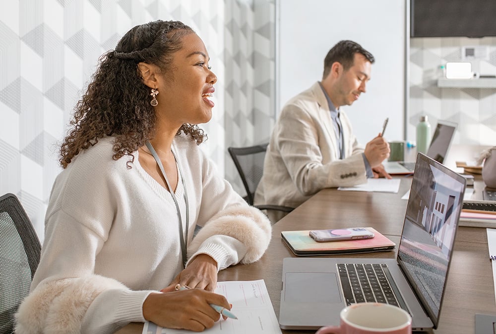 Two colleagues sit side by side, taking notes during a meeting.