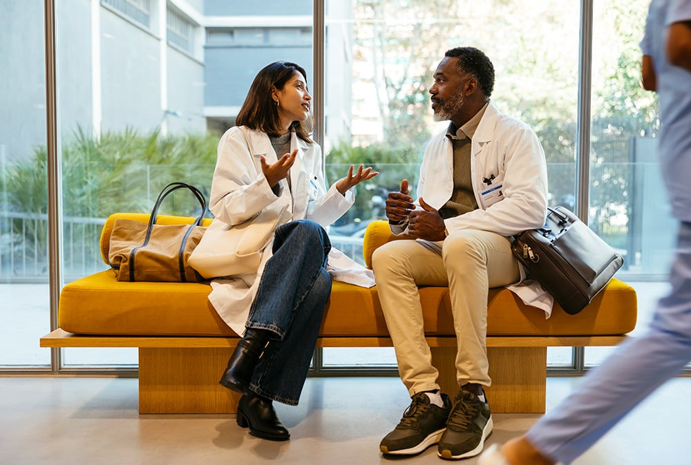 Two colleagues talking while sitting on a yellow ochre bench.